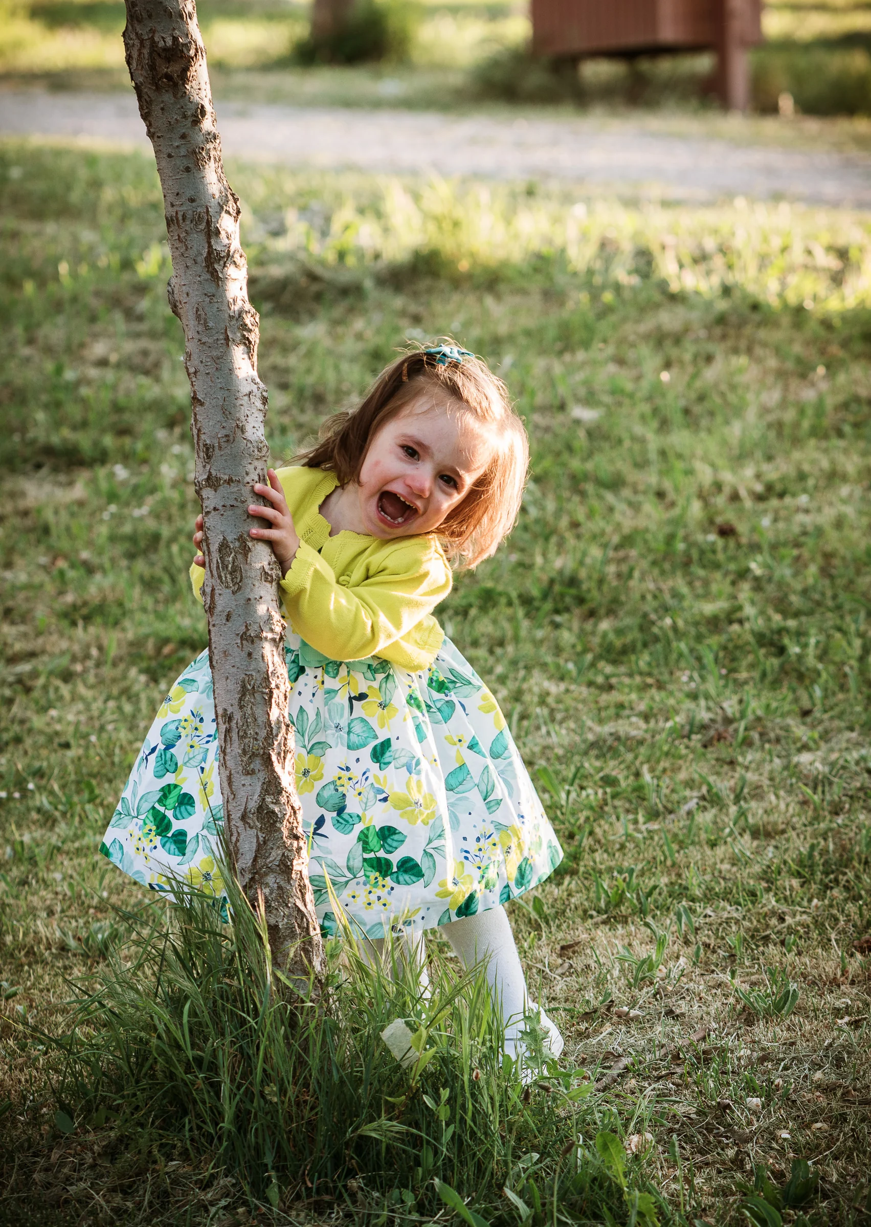 Niña pequeña juega alrededor de un árbol y sonríe durante una sesión infantil al aire libre.
