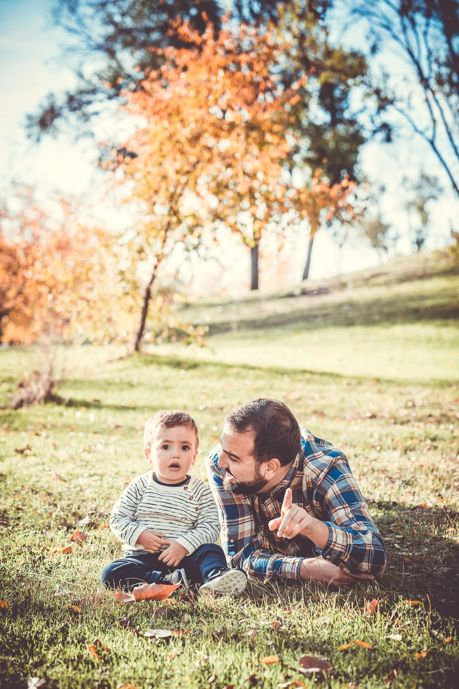 Padre se tumba junto a su hijo pequeño sobre la hierba durante una sesión familiar de otoño.