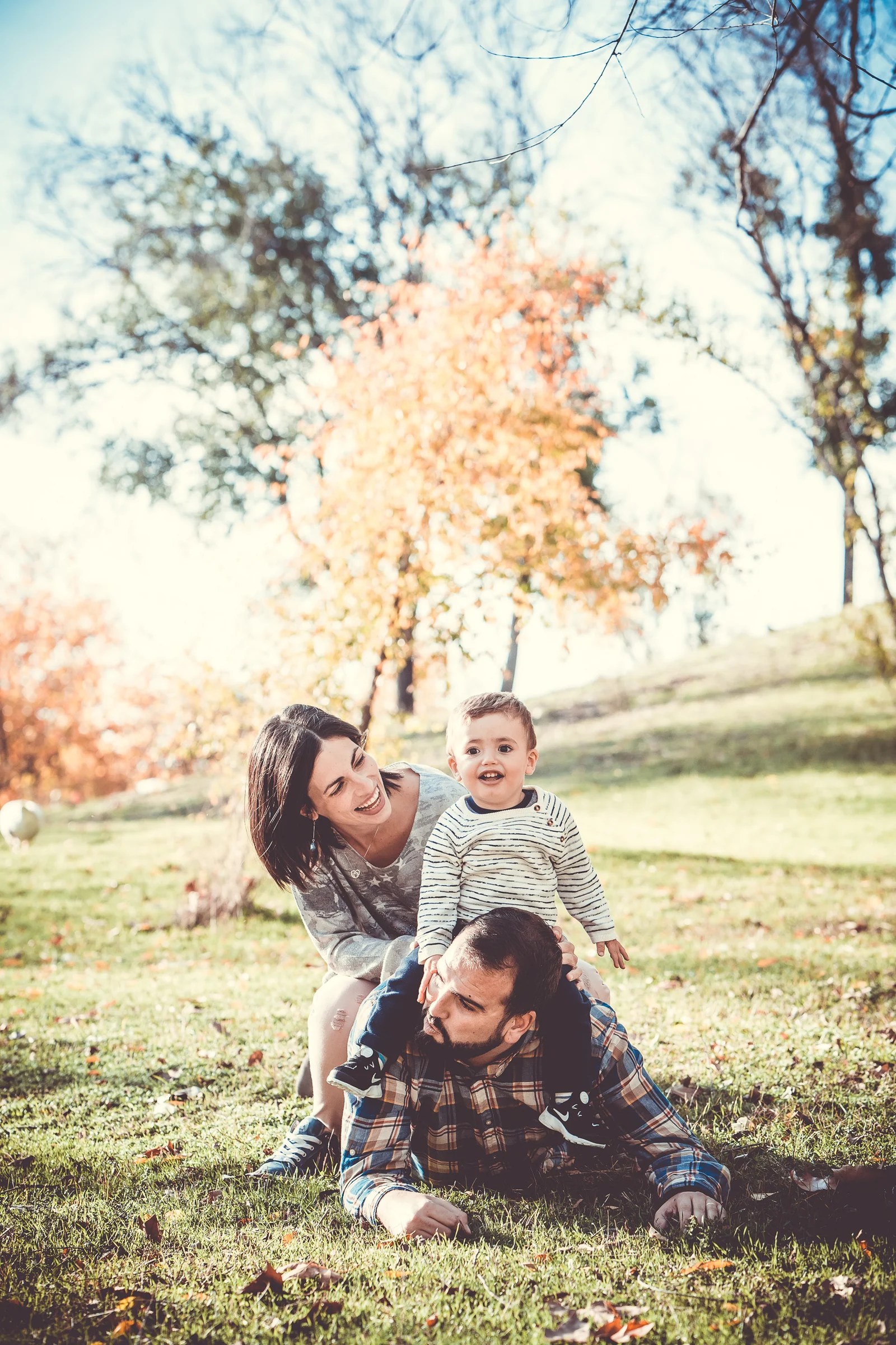 Madre, padre e hijo juegan juntos sobre la hierba en un parque de otoño.