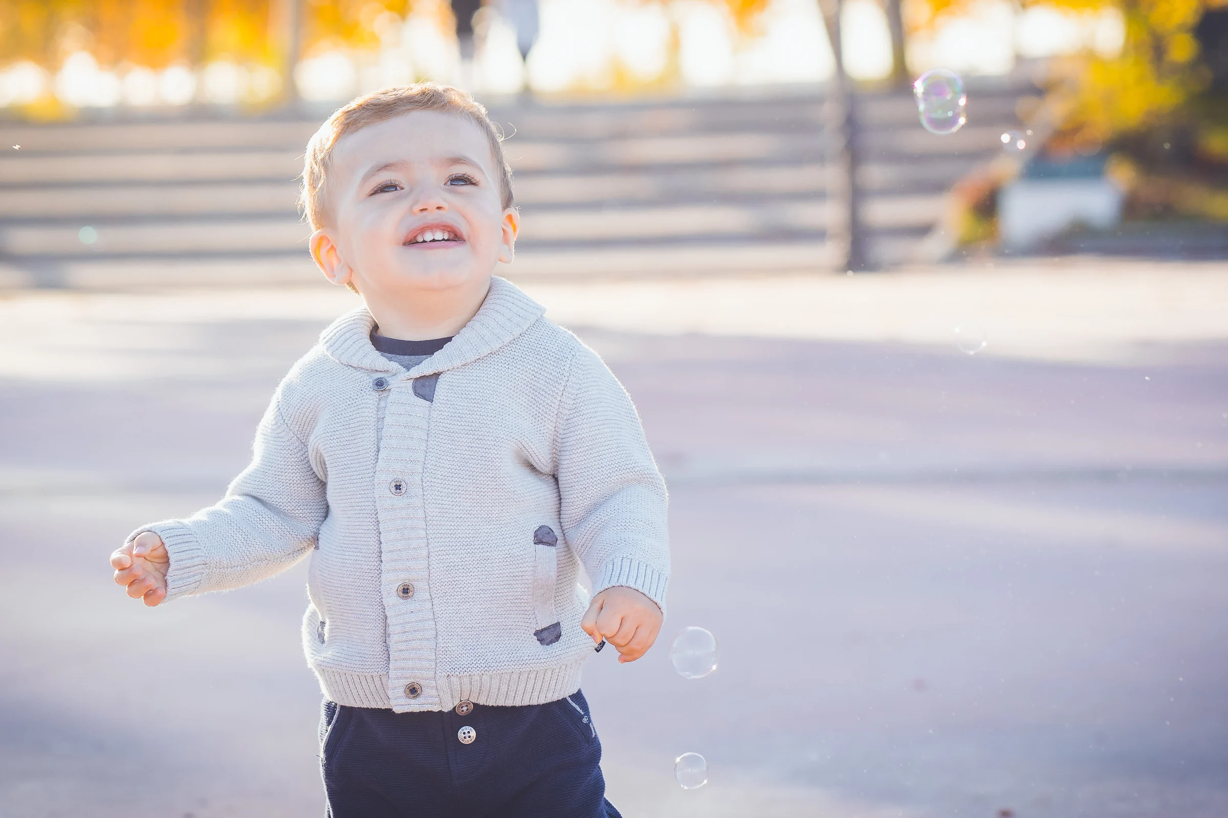 Niño pequeño sonríe mientras mira hacia arriba siguiendo unas burbujas de jabón.