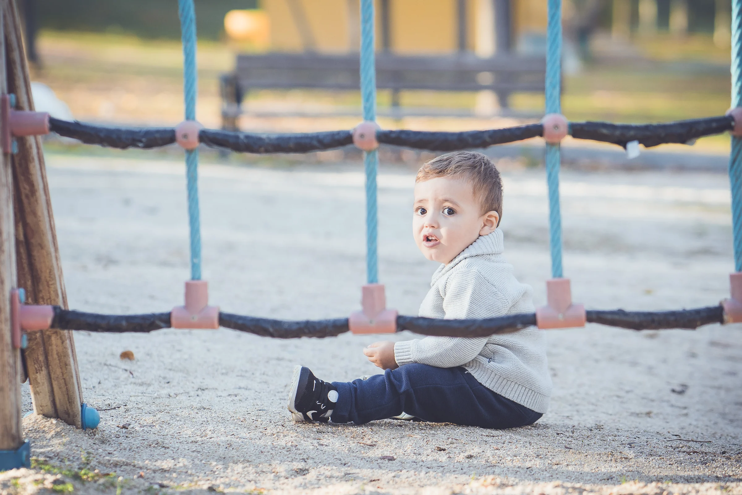 Niño pequeño está sentado detrás de una red de juegos y mira hacia la cámara.