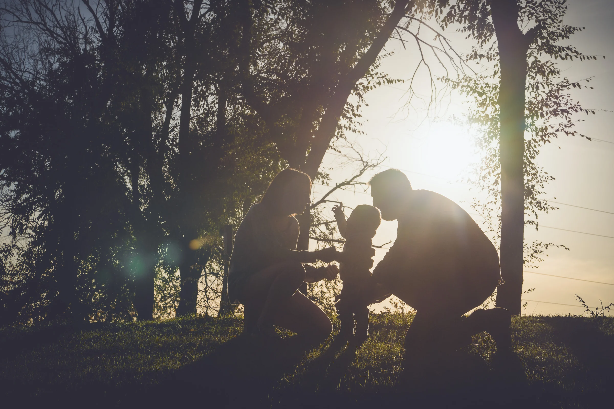 Siluetas de una madre, un padre y su hijo pequeño se recortan frente al sol del atardecer.