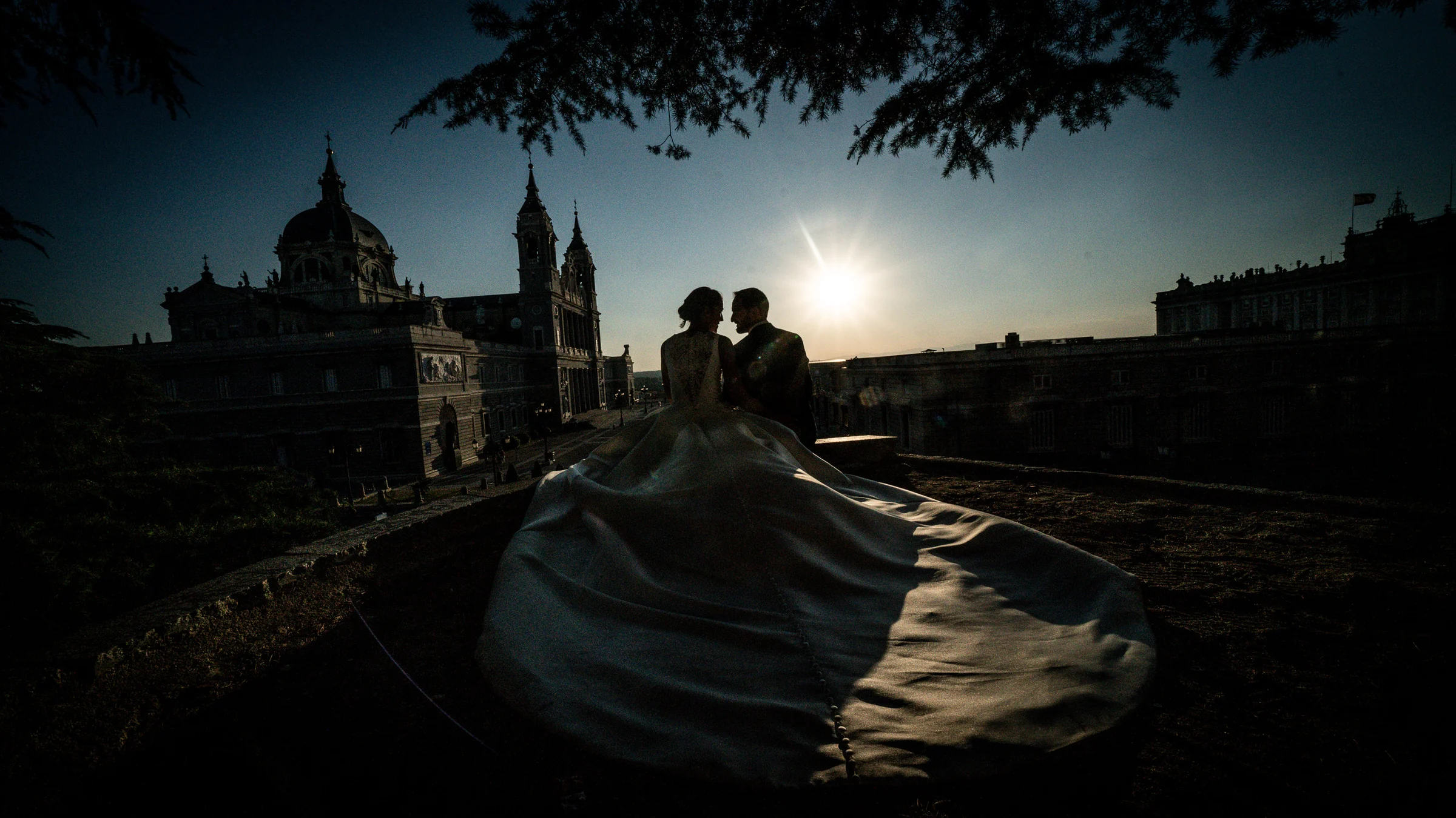 Silueta de Sara y Edu al atardecer frente a la arquitectura del Palacio Real y la Catedral de la Almudena en Madrid.