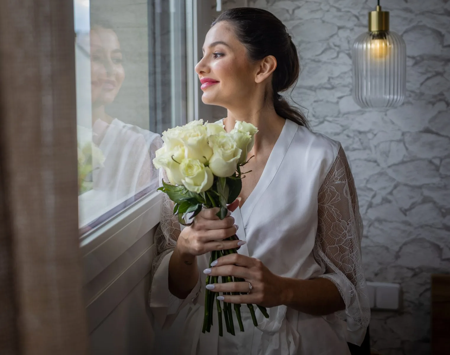 Novia con ramo junto a la ventana durante una boda en Valquijancho.